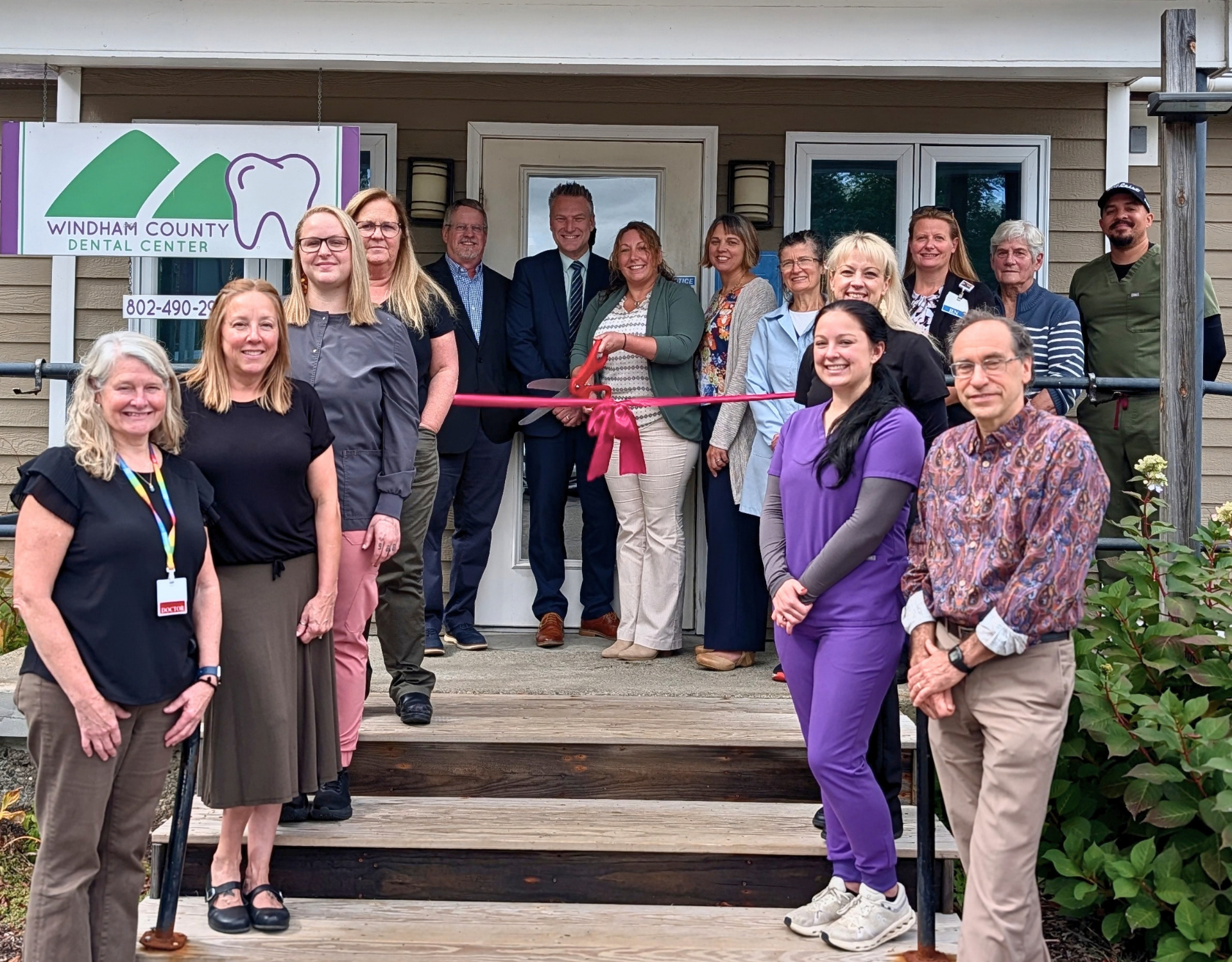 A group of people stands outside of a dental clinic cutting a ribbon