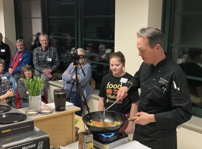 A chef stands at a cooking station with a wok