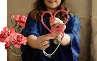 A stethescope being held in a heart shaped by a person wearing a blue graduation robe is framed by red carnation graphics,
