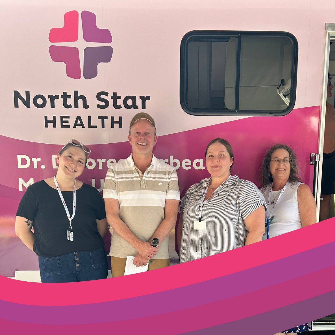 Four North Star staff stand in front of a pink mobile health clinic with "North Star HEALTH" written on the side.