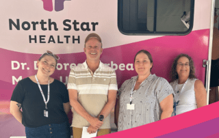 Four North Star staff stand in front of a pink mobile health clinic with "North Star HEALTH" written on the side.