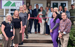 A group of people stands outside of a dental clinic cutting a ribbon