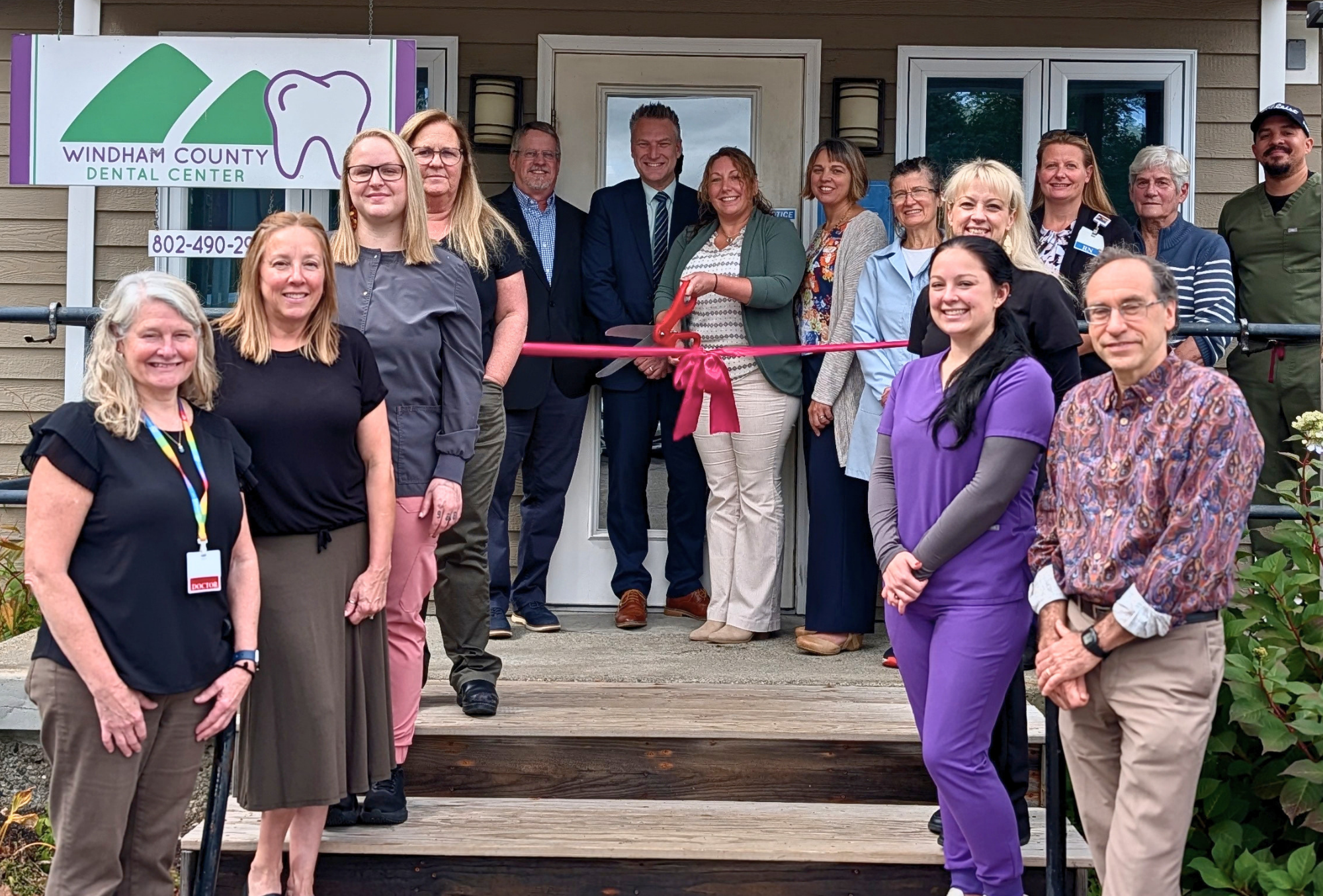 A group of people stands outside of a dental clinic cutting a ribbon
